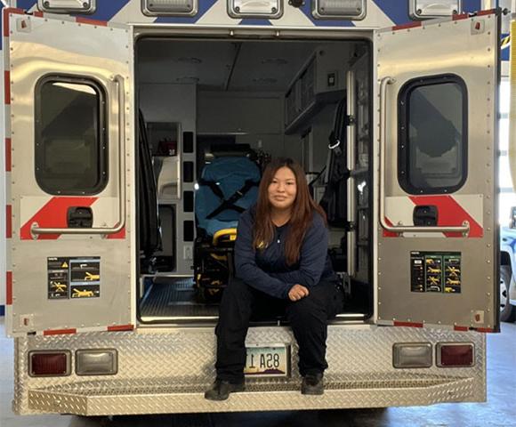 Tashawnee Wood dressed in EMT uniform sitting on back of ambulance with the doors open